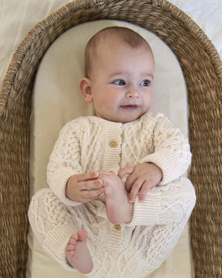 Baby in a moses basket wearing neutral knitted romper