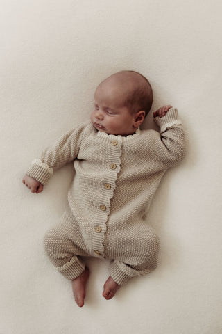 Sleeping baby wearing knitted beige romper with cream cuffs