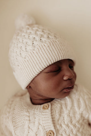 Baby wearing cream cable knit hat and cardigan