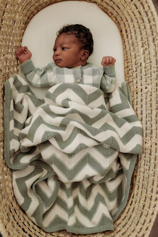 Baby in moses basket wearing sage and cream check romper and with sage and cream chevron stripe knitted blanket