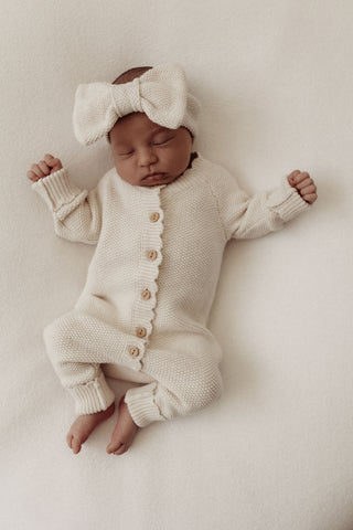 Sleeping newborn baby wearing knitted romper and bow headband