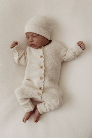Sleeping baby wearing neutral knitted hat and romper