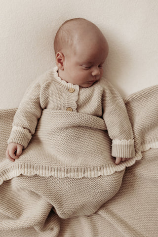 Sleeping baby wearing knitted beige romper with a knitted scallop edge baby blanket