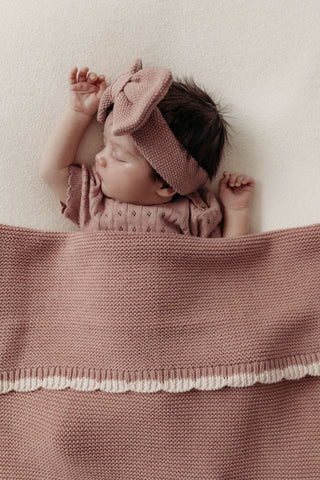baby girl sleeping with pink knitted bow headband and pink scallop edge blanket