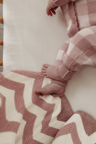baby feet wearing checkered knit romper, with a pink and cream chevron stripe blanket 
