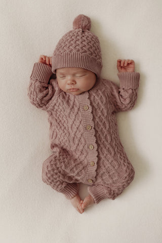Sleeping baby wearing pink cable knit hat and romper