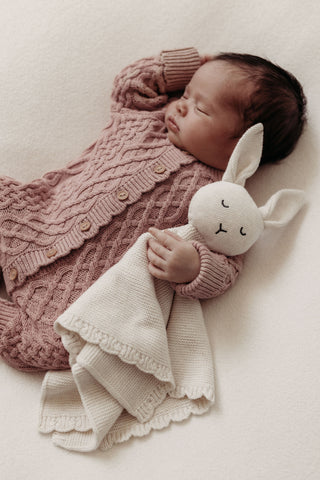 Newborn baby in cable knit romper cuddling bunny comforter