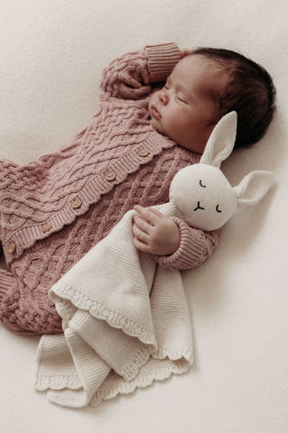 Newborn baby wearing pink cable knit romper cuddling knitted bunny comforter