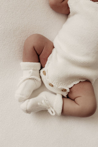 Baby wearing white knit romper and booties