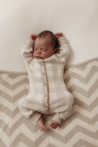 Sleeping baby wearing grey neutral check knitted romper lying on grey and cream chevron stripe knitted blanket