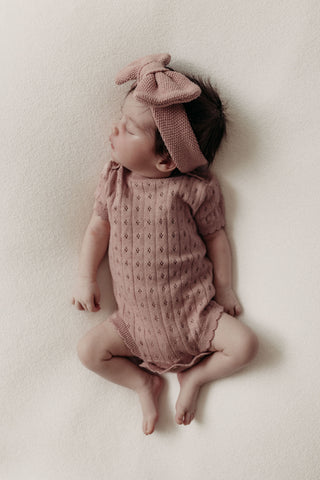 Sleeping baby wearing pink knitted bow headband and bodysuit