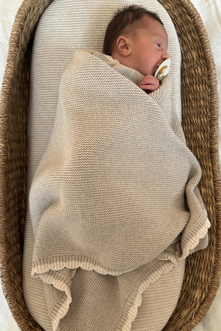 Baby in moses basket swaddled in knitted blanket