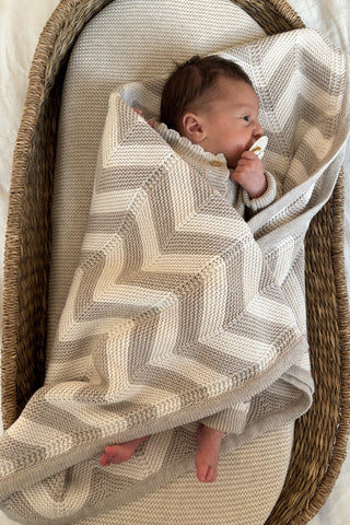 Baby in moses basket with dummy, swaddled in chevron stripe knitted blanket