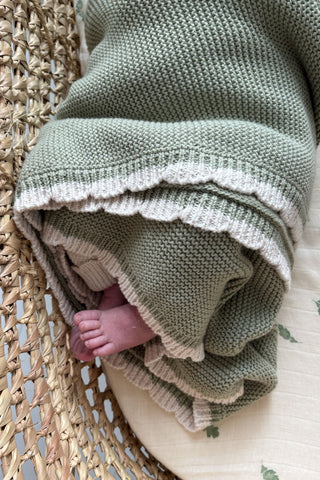 baby in moses basket swaddled in sage green blanket with cream scalloping detail
