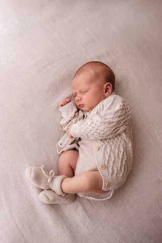 Sleeping baby wearing neutral knitted cardigan and booties
