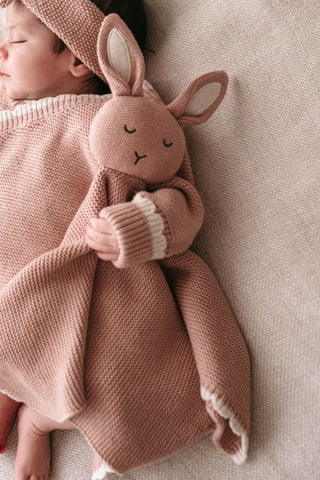 Baby cuddling a pink knitted bunny comforter