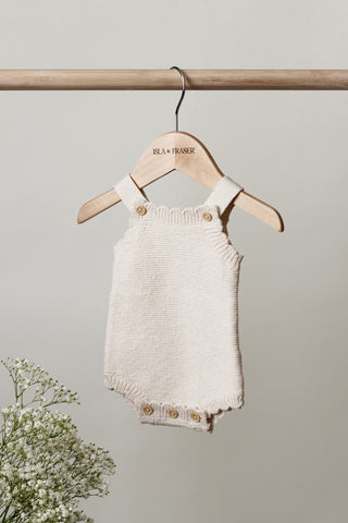 Knitted Baby Romper hanging on a wooden rail on an Isla & Fraser hanger with flowers
