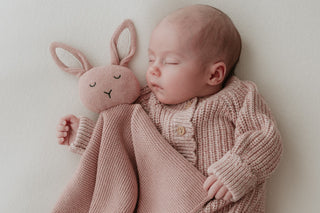 Sleeping newborn wearing a pink knitted romper with a pink knitted bunny comforter with cream ears