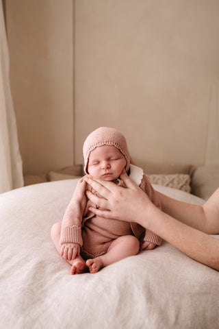 Sleeping baby sitting up, supported, wearing a pink knitted bonnet and cardigan