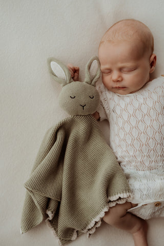 Baby wearing a white open knit bodysuit with a sage green knitted bunny comforter with white scalloped trim and ears 