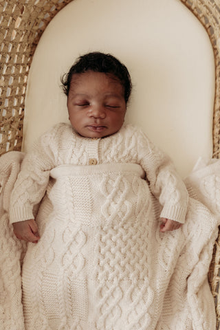 Sleeping baby in moses basket wearing cable knit cardigan and with a cable knit blanket