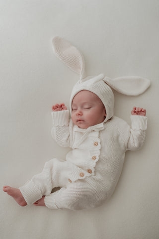 Baby wearing knitted bunny ear bonnet and romper in white 