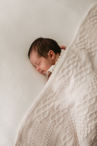 Smiling baby under a cable knit blanket