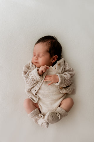 sleeping baby wearing a knitted grey cable knit cardigan, beige romper, and grey booties