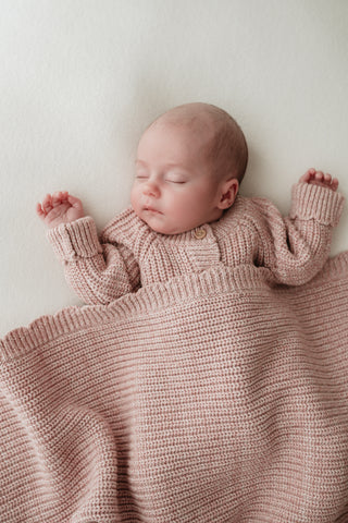 Sleeping baby wearing knitted pink romper and blanket with scalloped edge