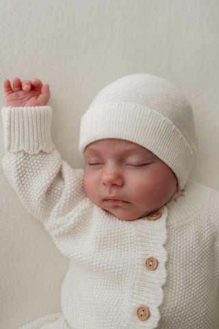 Sleeping baby wearing white knitted hat and romper