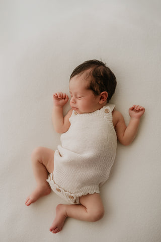Sleeping baby wearing neutral knitted romper with button fastening