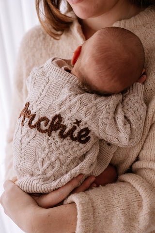 Newborn baby in mother's arms wearing a hand embroidered 'Archie' cable knit cardigan