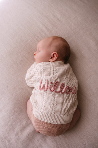 Sleeping baby wearing a hand embroidered 'Willow' named cable knit cardigan