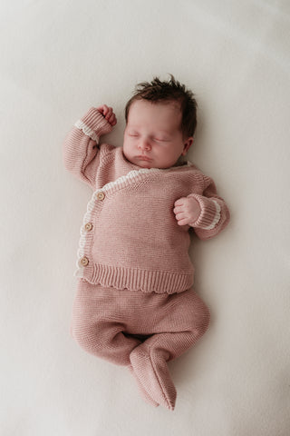 Baby wearing pink knitted wrap cardigan and footed trousers