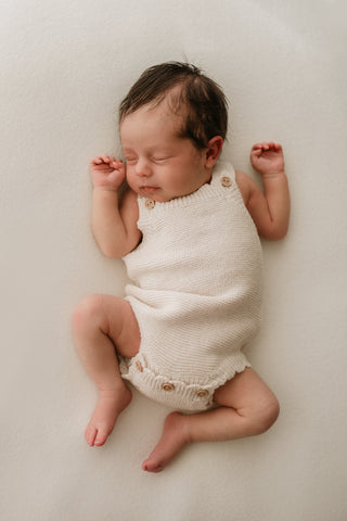 Sleeping baby wearing neutral knitted romper with button fastening