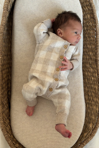 baby in moses basket wearing checkered knit romper
