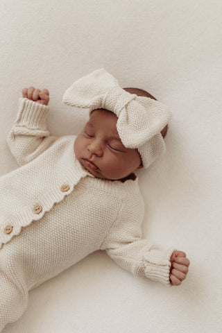 Newborn baby wearing a knitted bow headband and romper