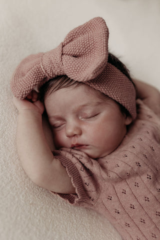 Sleeping baby wearing pink knitted bow headband