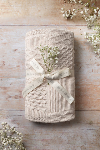 Cable Knit Blanket tied with an Isla & Fraser ribbon on a wooden backdrop with gypsophilia