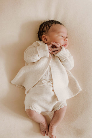 Baby clasping hands wearing neutral knitted outfit