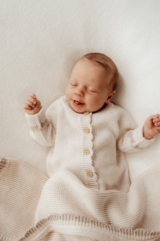 Newborn baby wearing a cream knitted romper with a beige scalloped edge and a matching blanket