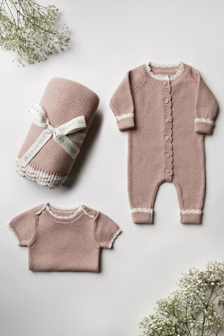Pink knitted blanket, romper and folded bodysuit with a cream scalloped edge.