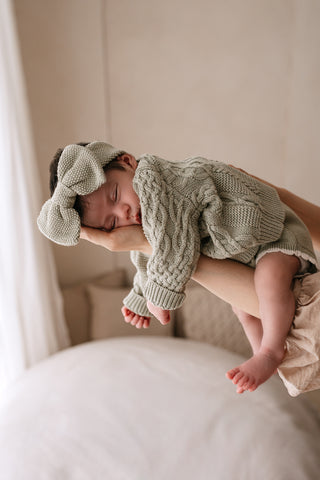 Sleeping newborn wearing sage green knitted outfit lying on mother's arms