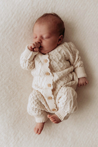 Sleeping baby wearing a neutral cable knit baby romper 