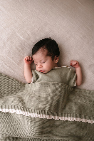 Sleeping baby wearing sage romper with a sage scalloped edge blanket