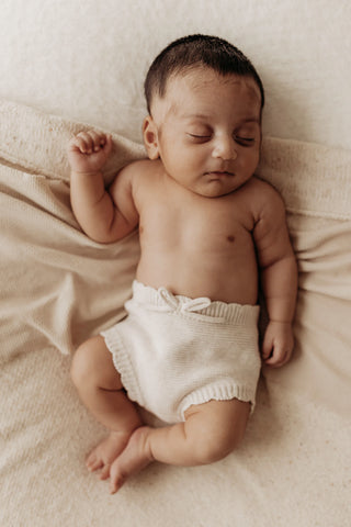 Sleeping newborn baby lying on beige blanket wearing knitted bow bloomers