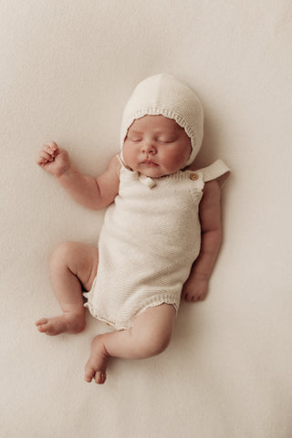 Baby wearing knitted romper and bonnet
