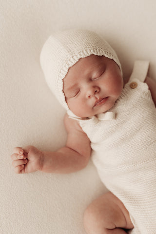Baby wearing neutral knitted bonnet and romper