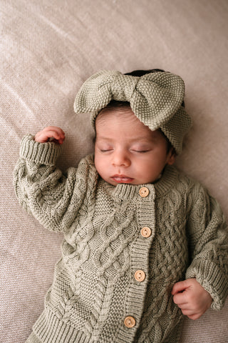 Baby wearing sage cable knit cardigan and bow headband