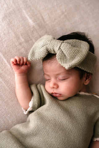 Sleeping newborn wearing sage green bow headband and sage romper